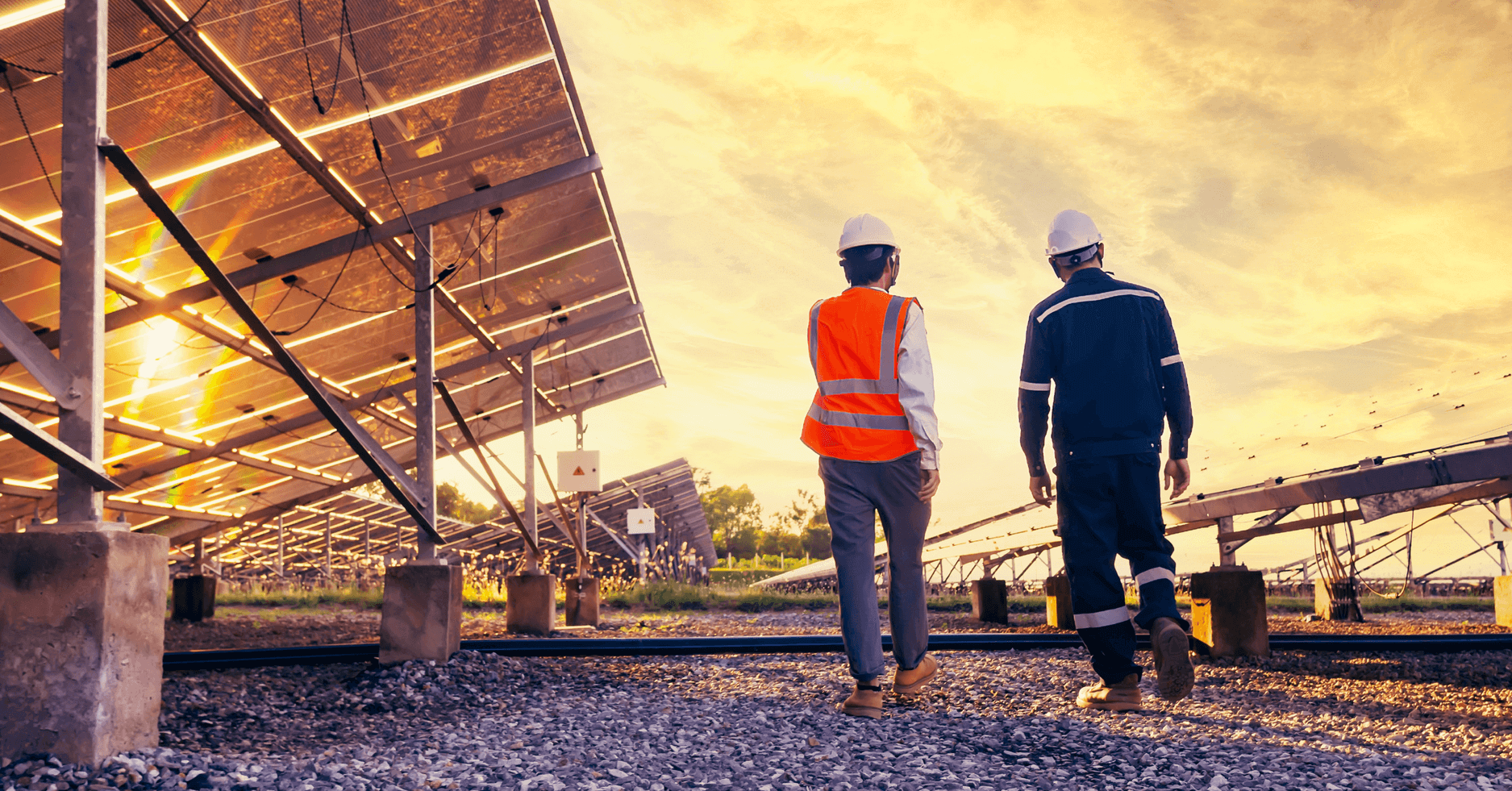 Two workers walk outside through a solar farm, in between two solar panels